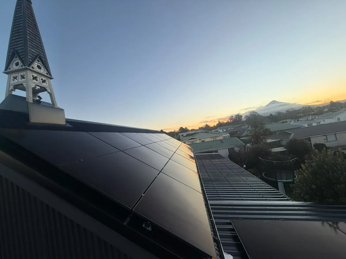 A 14.3kW EFS Solar array beside a church steeple in Stratford, Mount Taranaki at sunset behind